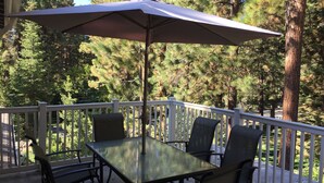 Une terrasse extérieure avec une table et des chaises en verre, un parasol et une balustrade blanche.