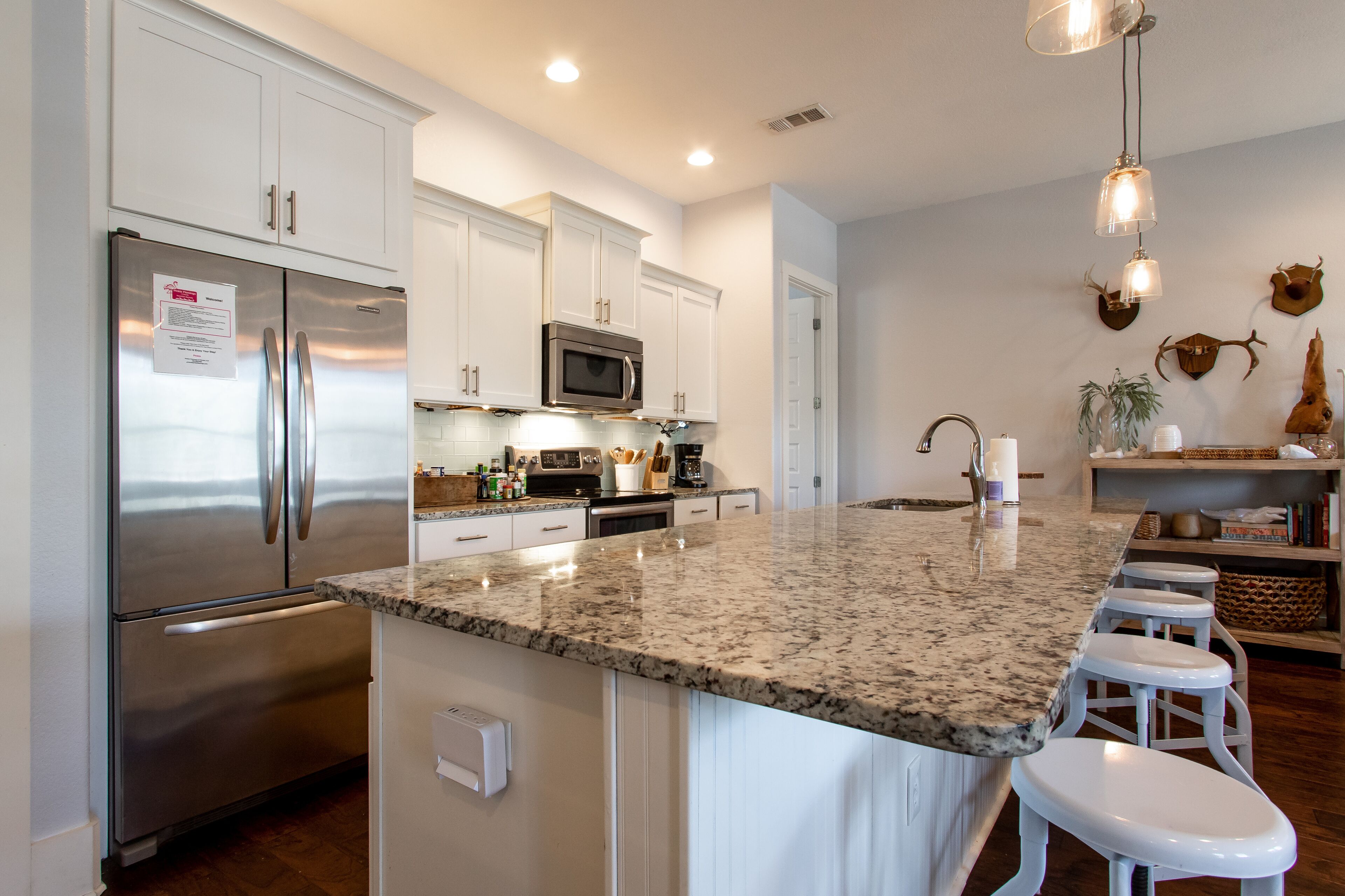 A modern kitchen with white cabinets, stainless steel appliances, a granite countertop, and bar stools.