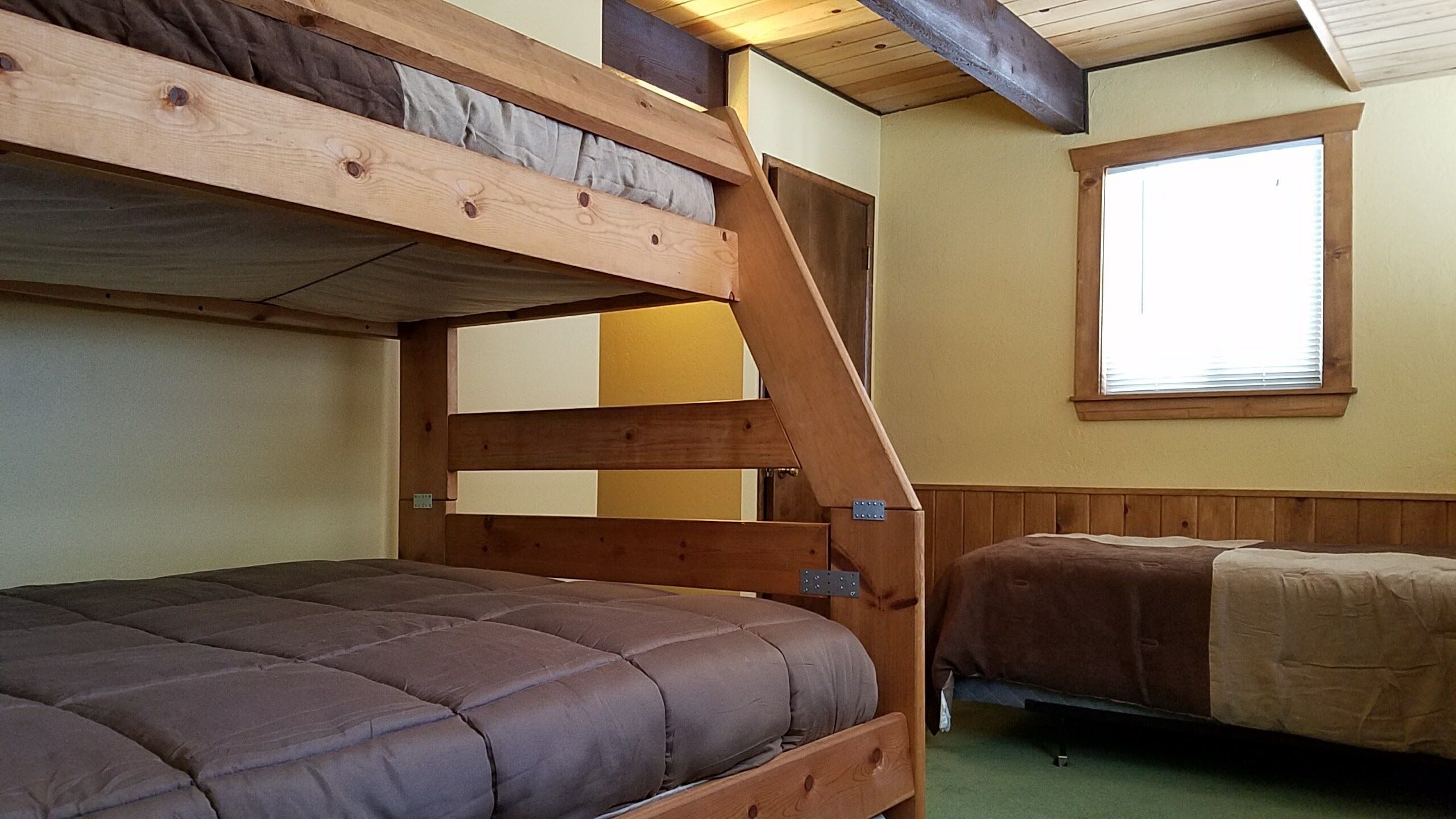 Une chambre avec un lit superposé, une fenêtre et des poutres en bois au plafond.