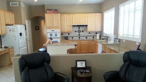 A compact living space with a kitchenette, two leather chairs, a small table with a clock, and a window with blinds. - Estrella's NASCAR HOT SPOT! FALL GOLF GETAWAY! HOLIDAY PLAY! (Goodyear)