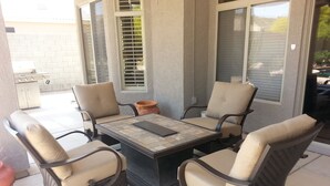 A patio with four wicker chairs and a square table, a small potted plant, and a grill. - Estrella's NASCAR HOT SPOT! FALL GOLF GETAWAY! HOLIDAY PLAY! (Goodyear)