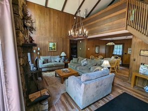 Een gezellige woonkamer met houten wanden, een kroonluchter en een eethoek met houten stoelen en een tafel.