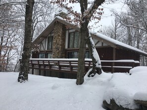 Een chalet met een stenen schoorsteen, houten terras en besneeuwde omgeving.