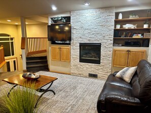 A living room with a stone wall, a fireplace, a television, and a bookshelf.