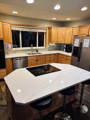A modern kitchen with wooden cabinets, a stainless steel refrigerator, a built-in oven, and a bar stool area.