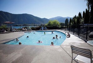 A swimming pool with people in it, surrounded by a fence, with mountains in the background.