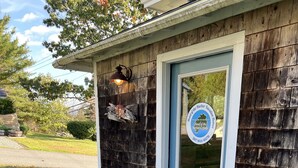Une cabane en bois avec une porte bleue, un petit porche et un paillasson bleu à l’entrée.