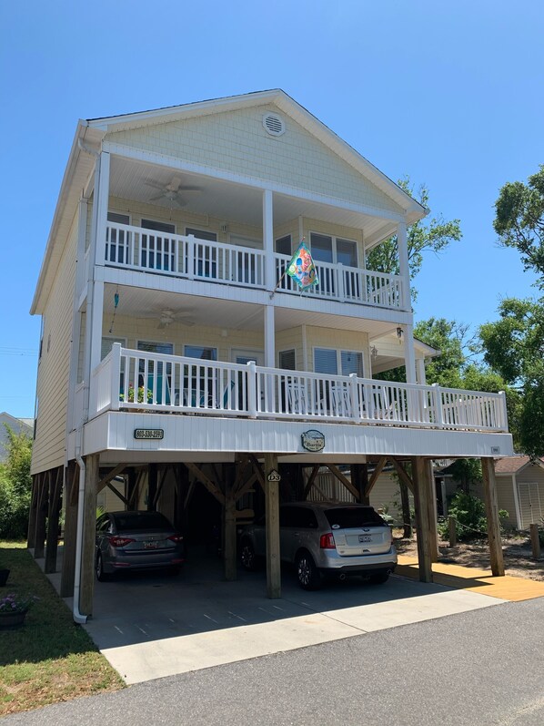 A two-story building with a balcony on the upper floor, a sign indicating a business, and a parking area with two cars. - Beautiful Ocean Lakes Beach Home......100 Yards to the Beach. (Myrtle Beach)