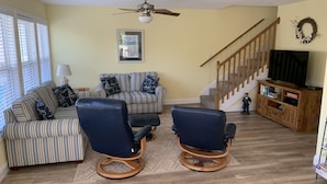 A living room with a striped sofa, two blue chairs, a ceiling fan, a staircase, and a wooden entertainment center. - Beautiful Ocean Lakes Beach Home......100 Yards to the Beach. (Myrtle Beach)