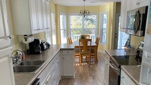 A kitchen with white cabinets, a wooden dining table, and a view of the outdoors through large windows. - Beautiful Ocean Lakes Beach Home......100 Yards to the Beach. (Myrtle Beach)