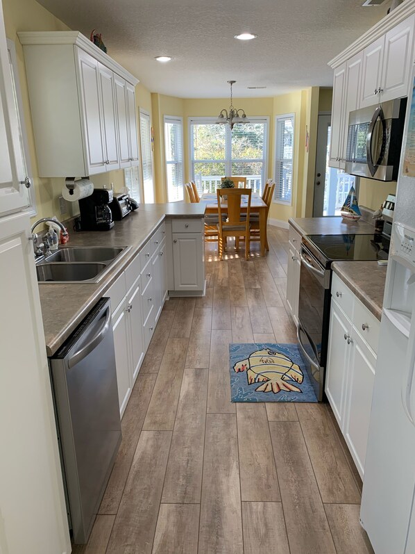 A kitchen with white cabinets, a wooden dining table, and a view of the outdoors through large windows.