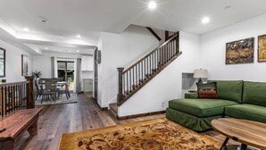 Ein geräumiger Wohnbereich mit einer Holzbank, einem grünen Sofa, einem gemusterten Teppich und einer Treppe.