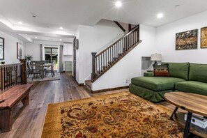 Ein geräumiger Wohnbereich mit einer Holzbank, einem grünen Sofa, einem gemusterten Teppich und einer Treppe.