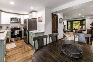 Uma cozinha moderna com armários brancos, eletrodomésticos de aço inoxidável e uma sala de jantar com mesa e cadeiras de madeira.