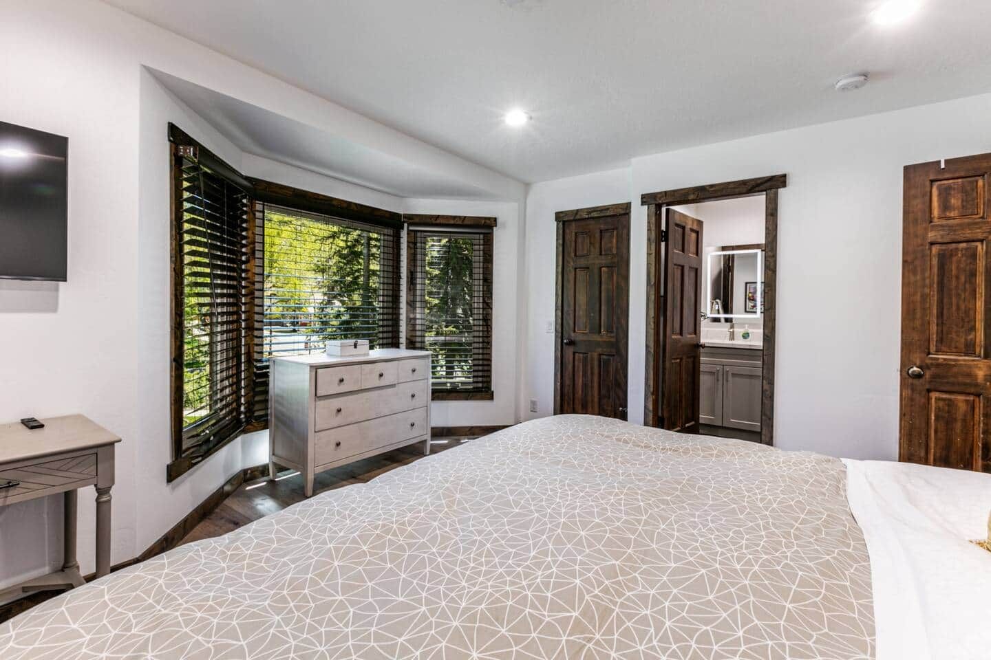 Un dormitorio con cama, cómoda, televisor y baño con espejo.