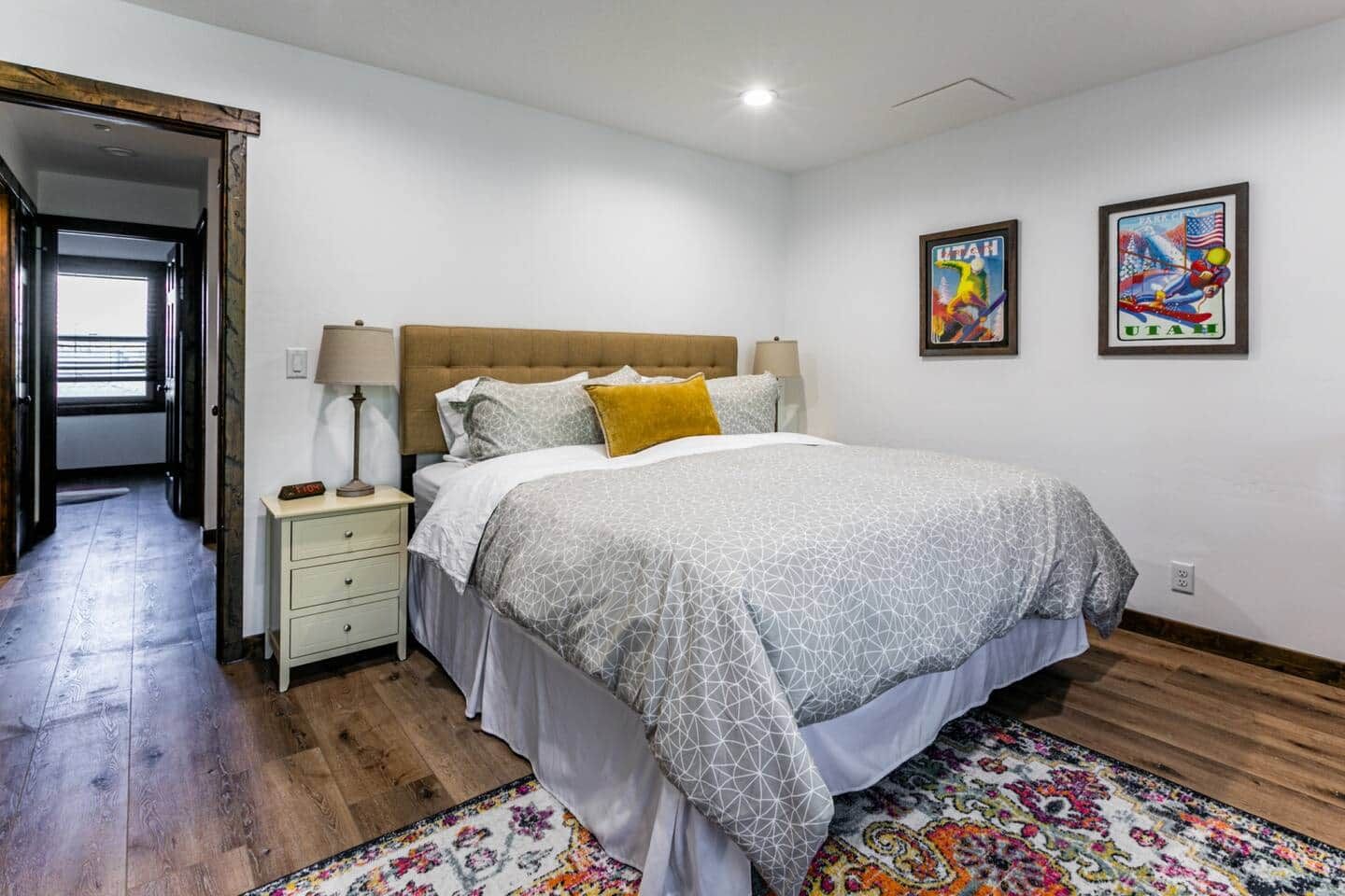 Quarto com cama, mesa de cabeceira, abajur e duas imagens emolduradas na parede.