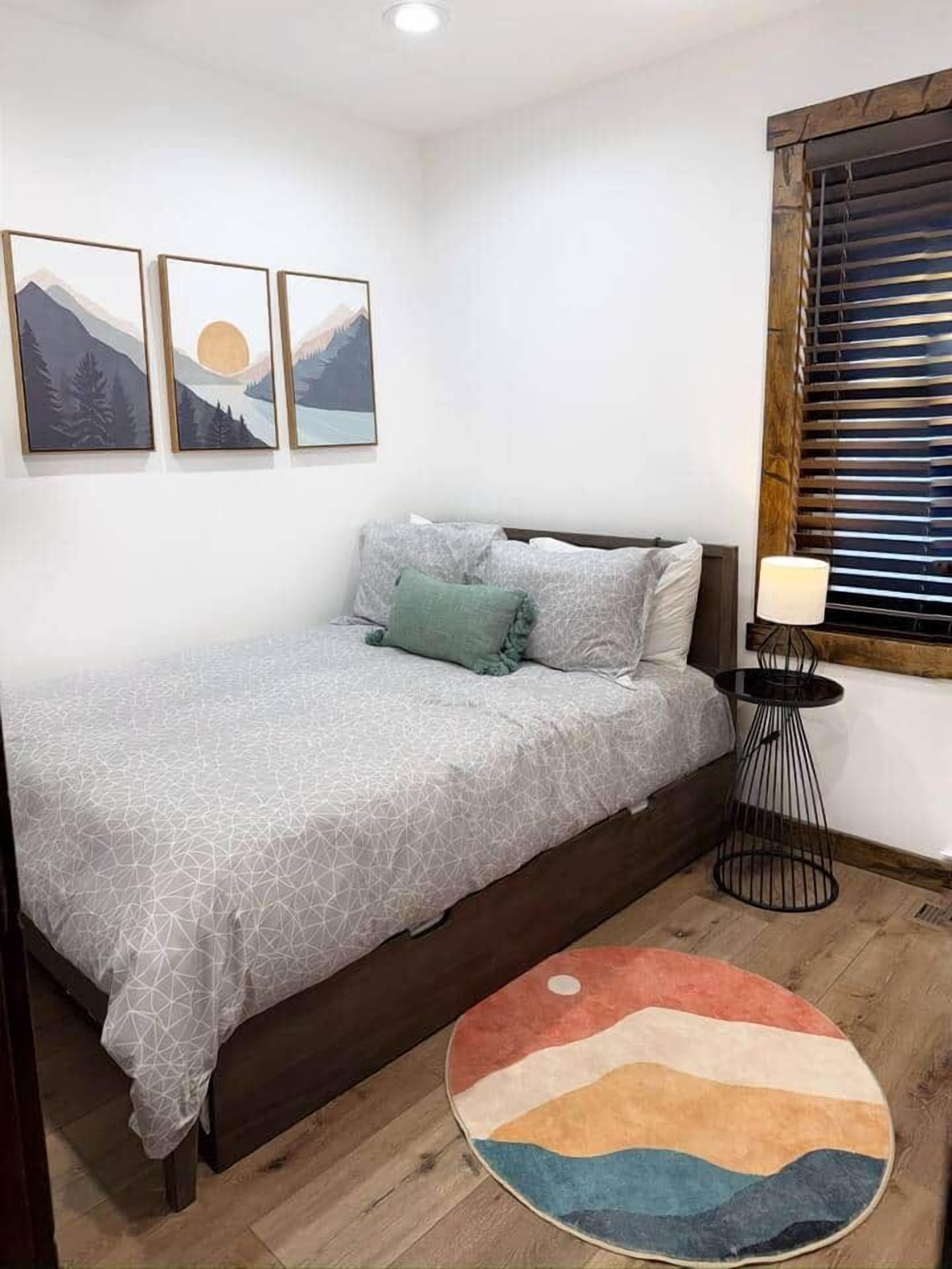 Ein Schlafzimmer mit einem Bett, einem runden Teppich, einer Wandlampe und drei gerahmten Bildern.
