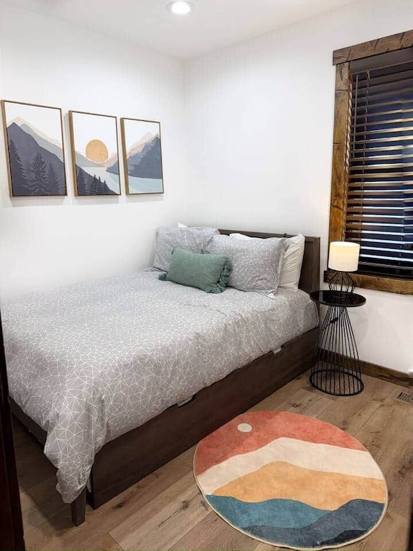 Quarto com cama, tapete redondo, luminária na parede e três quadros emoldurados.