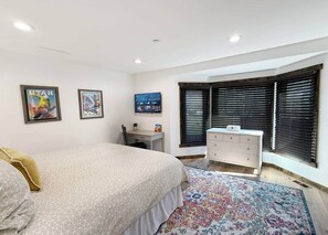 Ein Schlafzimmer mit Bett, Schreibtisch, Kommode und Fenster mit Jalousien.
