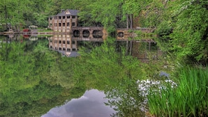 Una cabaña junto al lago con un puente de piedra y su reflejo en el agua.