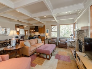 A spacious living room with a fireplace, comfortable seating, and a kitchen area in the background.
