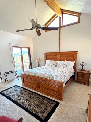 Ein Schlafzimmer mit einem hölzernen Bett, einem Deckenventilator, einem Nachttisch und Blick ins Freie.