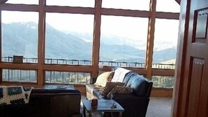 A room with a large window offering a mountain view, a dark leather sofa, a small table, and a wooden door. - Spectacular views and rural life, yet close to Boise (Boise)