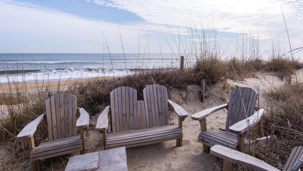 Drie houten Adirondack-stoelen op een zanderig strand, met uitzicht op de oceaan.