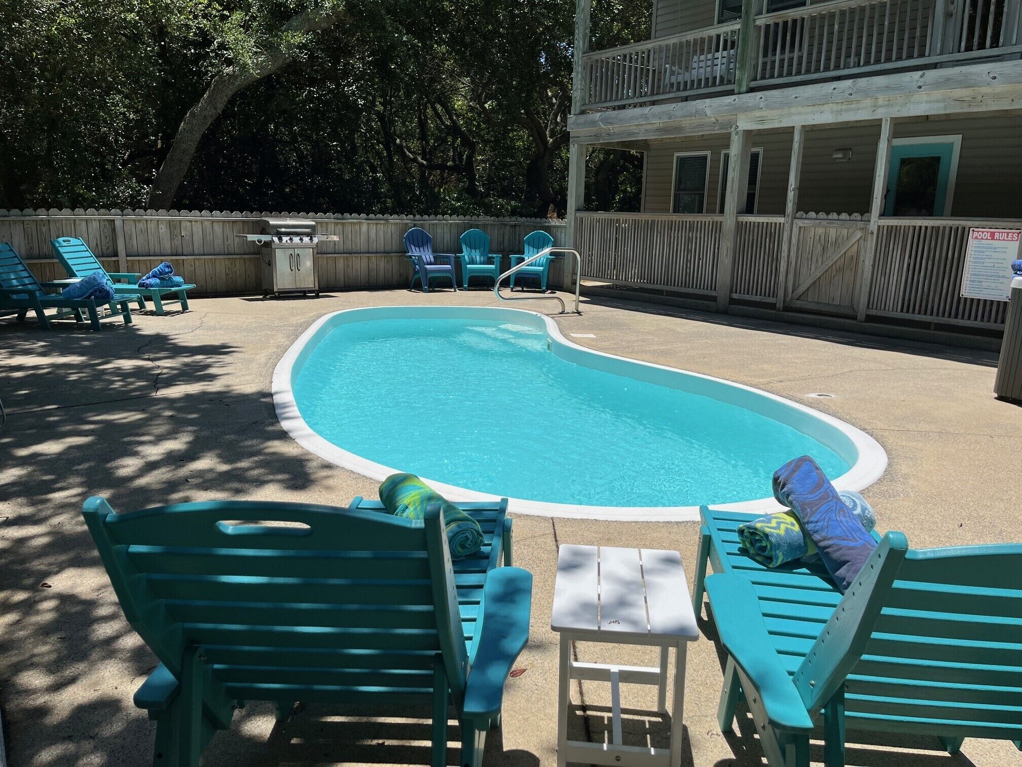 A swimming pool with blue chairs and a small table, surrounded by a wooden fence.