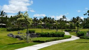 A well-maintained grassy area with a curved pathway, palm trees, and a clear blue sky. - Fairways 1706 - Renovated, includes Beach Access, Bikes (Kamuela)