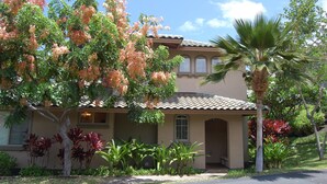 A two-story house with a tiled roof, a covered porch, and a well-maintained garden with various plants and a palm tree. - Fairways 1706 - Renovated, includes Beach Access, Bikes (Kamuela)