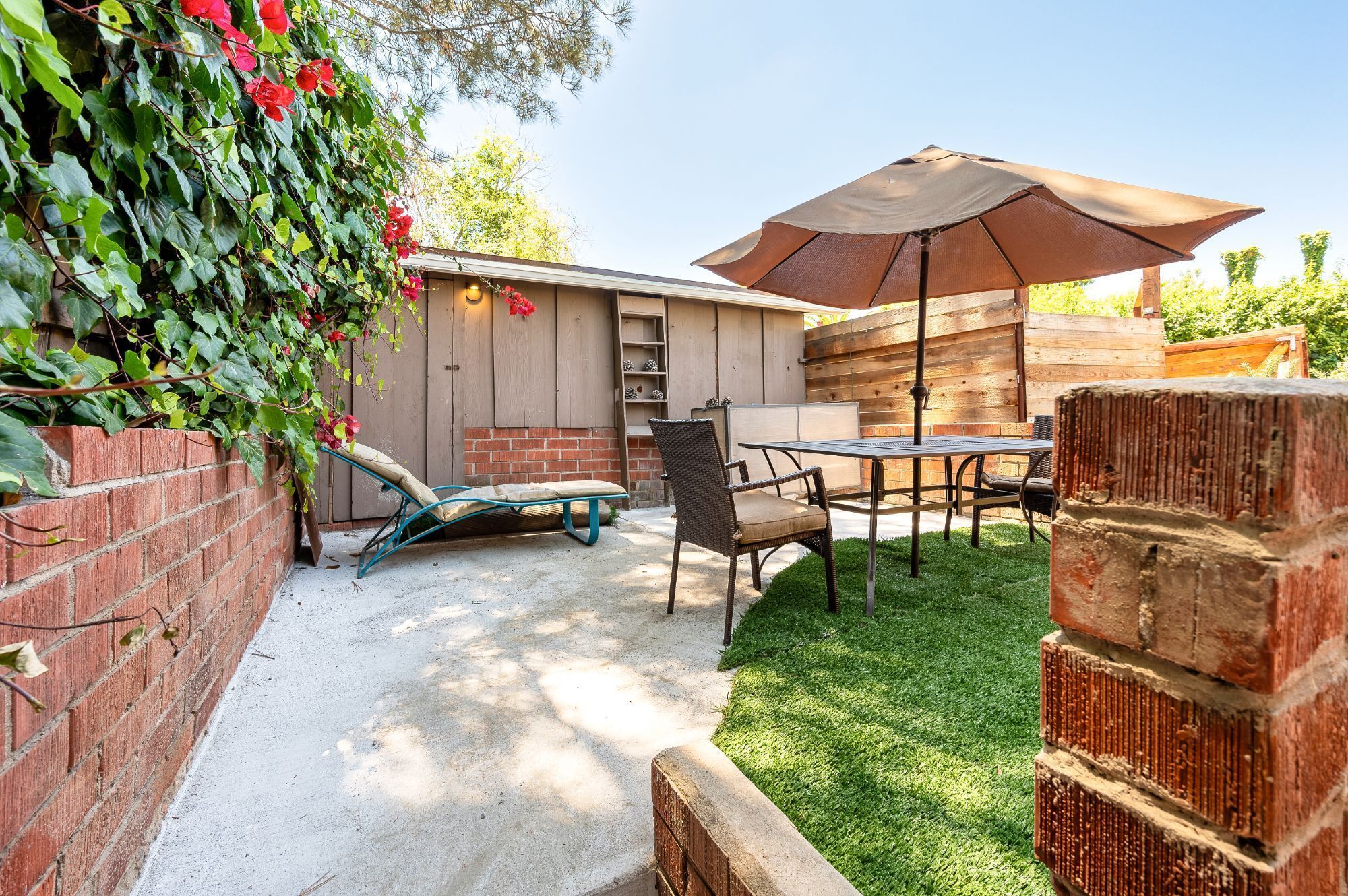 Un patio con una mesa, sillas, un muro de ladrillo y una cerca de madera.