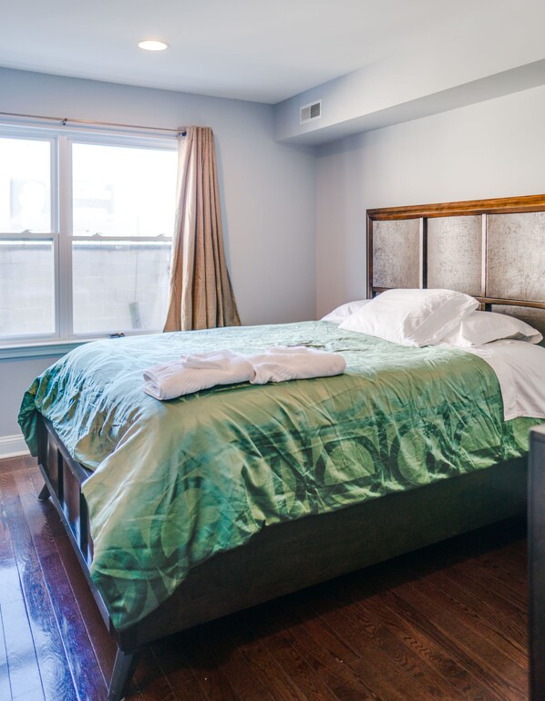 A neatly made bed with a green and white bedspread, a wooden headboard, and a window with curtains. - Roomy, 4BD/2.5Bth, Amazing Rooftop Deck and Large Patio (Philadelphia)