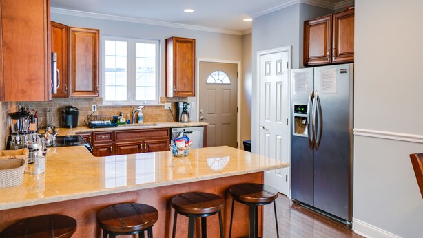 A kitchen with wooden cabinets, a stainless steel refrigerator, a large island with stools, and a window with a view.
