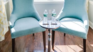 A room with two light blue armchairs facing a large window with a view of buildings and trees. There is a small round table with two water bottles and a book between the chairs.