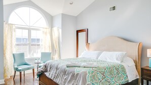 A bedroom with a large bed, a chair, a small table, and a window with curtains.