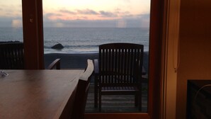 Una mesa de madera y dos sillas mirando a una playa con vista al océano y un cielo nublado.