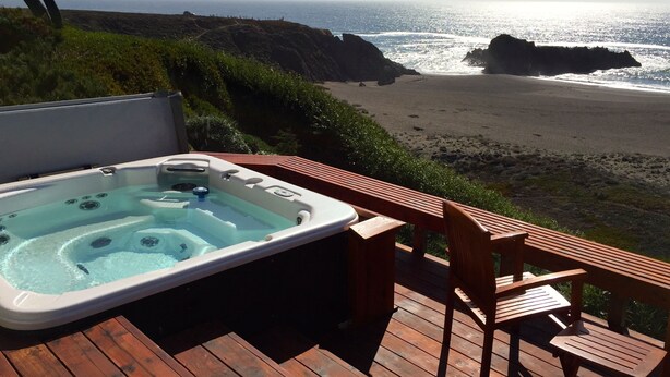 Un jacuzzi en una terraza de madera con vista a la playa y al océano.
