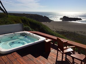Un bain à remous sur une terrasse en bois, avec vue sur la plage et l’océan.