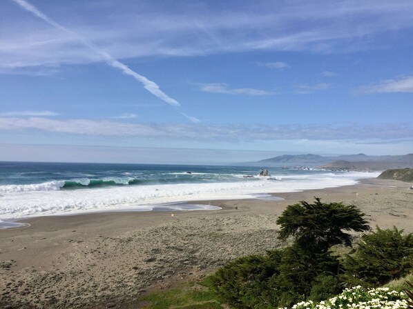 Une plage avec des vagues, un ciel dégagé et des montagnes à l’horizon.