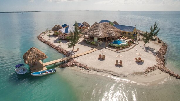 Un resort tropical con bungalows de techo de paja, una piscina y un muelle con barcos.