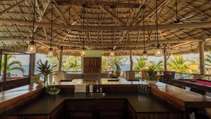 Un restaurante con techo de paja, muebles de madera y vistas al mar.