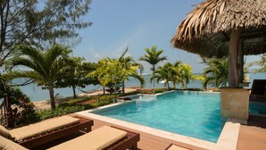 Zona de piscina con sillones de descanso, una estructura de techo de paja y vista al océano.