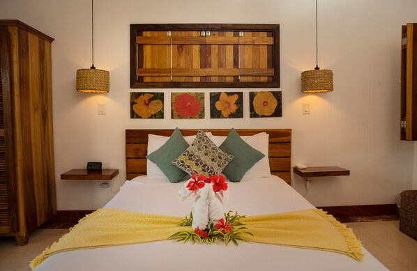 Habitación de hotel ordenada con cama, cabecera de madera, dos mesitas de noche y un panel de madera fijado a la pared sobre la cama.