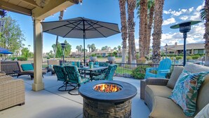 An outdoor patio with a stone fire pit, green chairs, and a covered table area. - BEST in Monterey Country Club-South-New Remodel-2024-STR or monthly-185 Gran Via (Palm Desert)