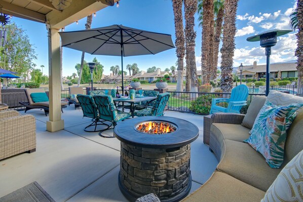 An outdoor patio with a stone fire pit, green chairs, and a covered table area.