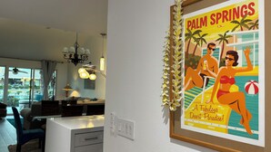 A framed poster of Palm Springs with a beach scene, a modern kitchen with a dining area, and a chandelier. - BEST in Monterey Country Club-South-New Remodel-2024-STR or monthly-185 Gran Via (Palm Desert)