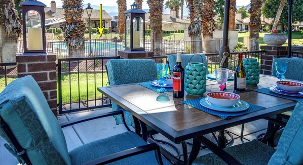 An outdoor patio with a pool view, featuring a table set with dinnerware, a bottle, and a decorative bowl.