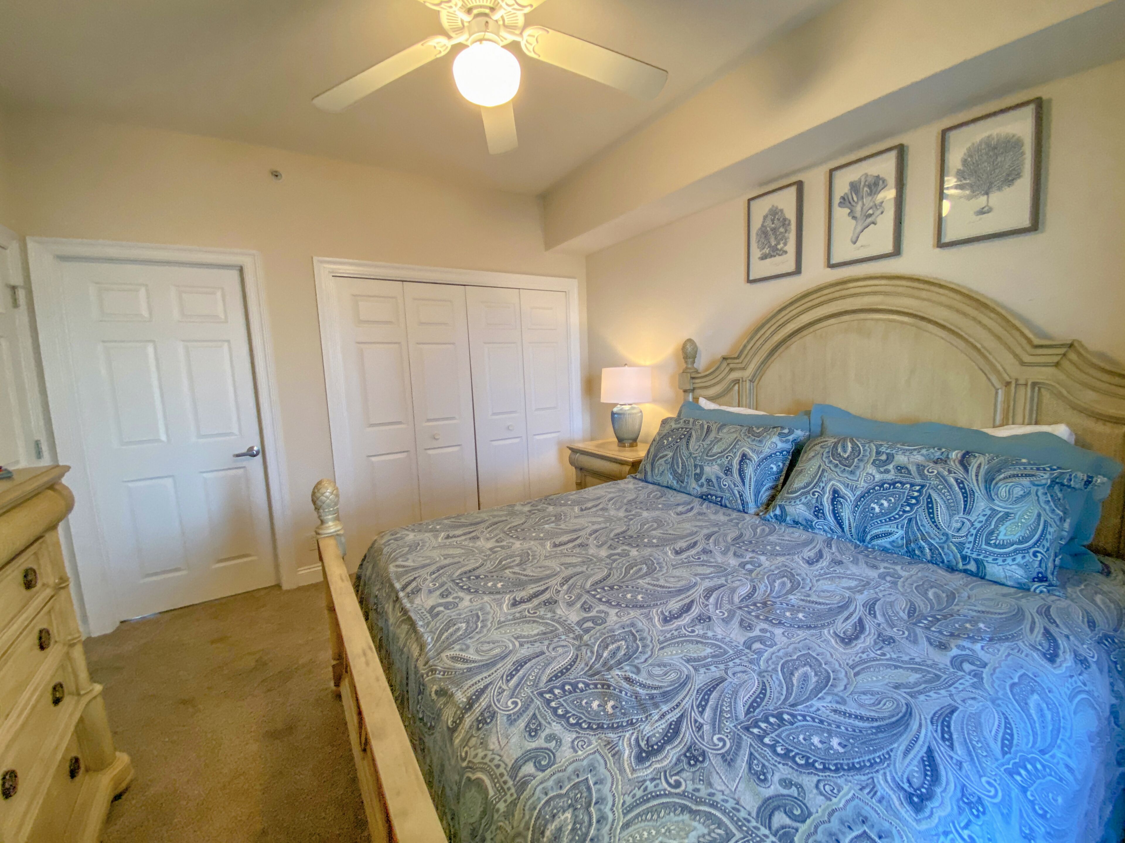 A bedroom with a bed, dresser, closet, and ceiling fan.