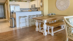 Une cuisine avec des meubles blancs, un réfrigérateur en acier inoxydable et une table à manger en bois, accompagnée de tabourets de bar.